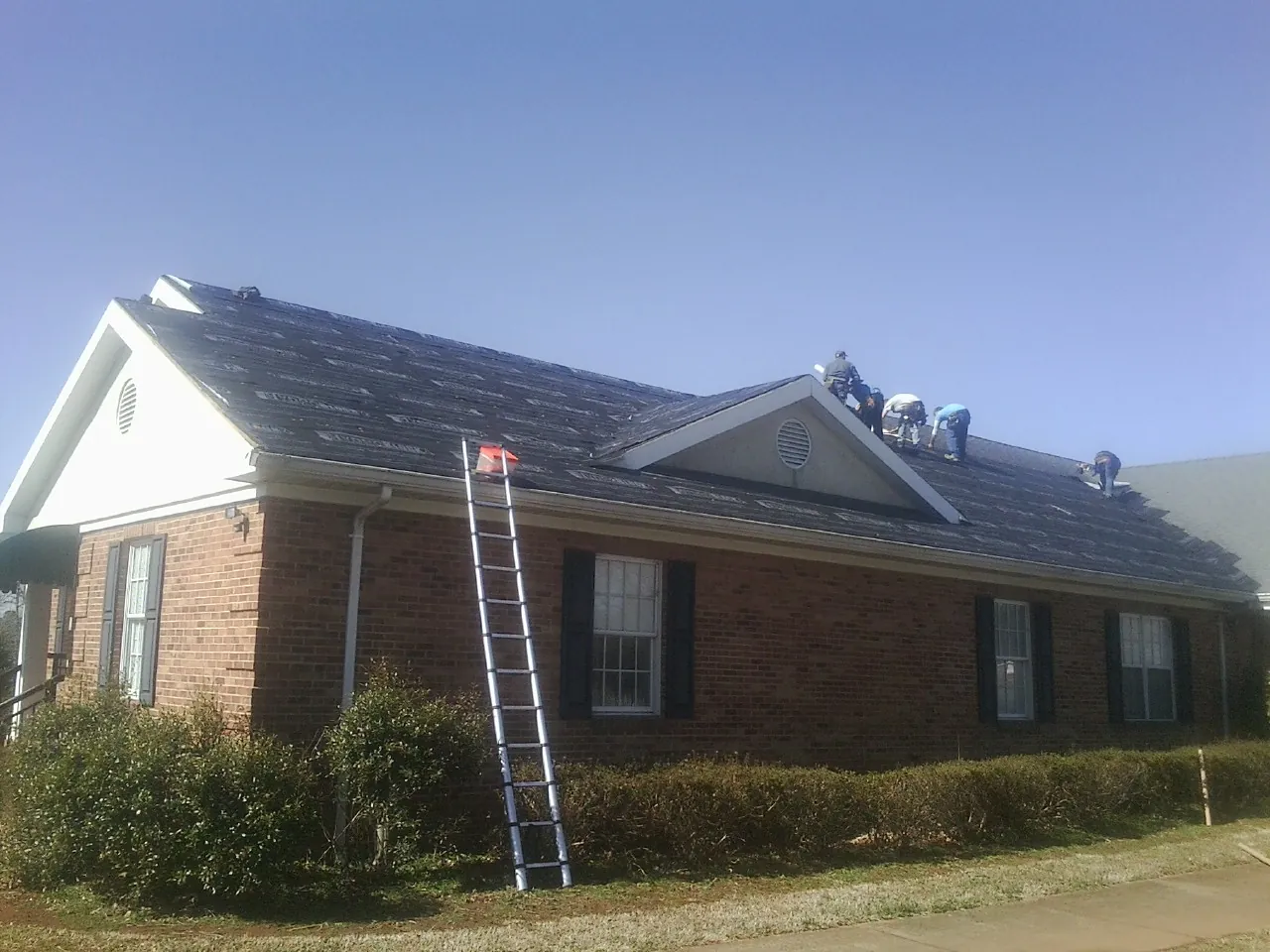 Crew tearing shingles off a brick ranch roof with a ladder set — Metal Roof Repair work by our crew in Brecksville