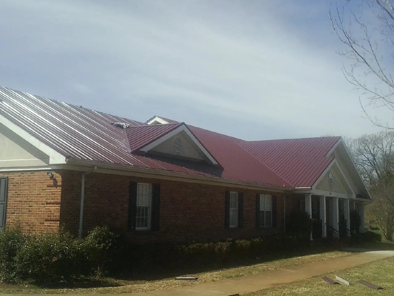 Red metal roof with gabled entries on a long brick building, from a Hail Damage Roof Repair job in Brecksville