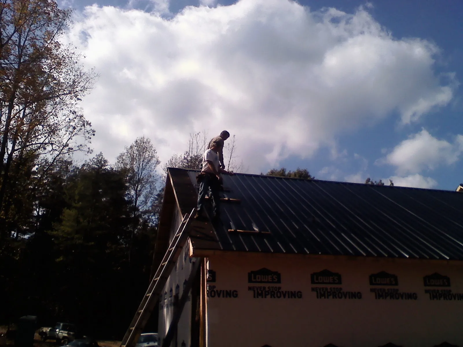Roofer fastening dark metal panels high against a cloudy sky, from a Roof Inspection job in Brecksville