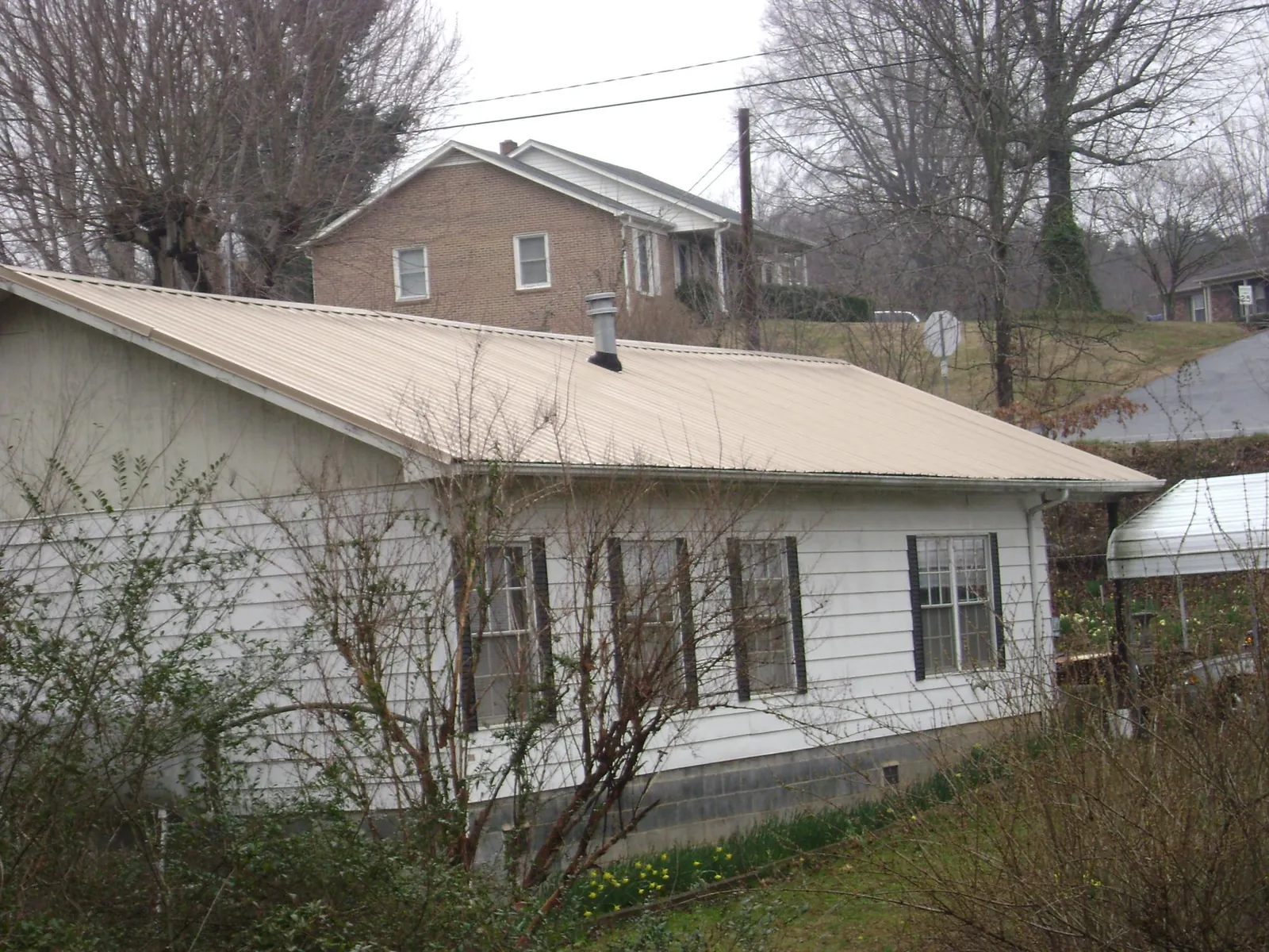 Tan metal roof on a white sided house set into a hillside — Commercial Roofing by Roofing Brothers in Brecksville